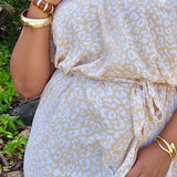 Woman wearing a beige and white leopard print long summer dress with gold accessories outdoors.