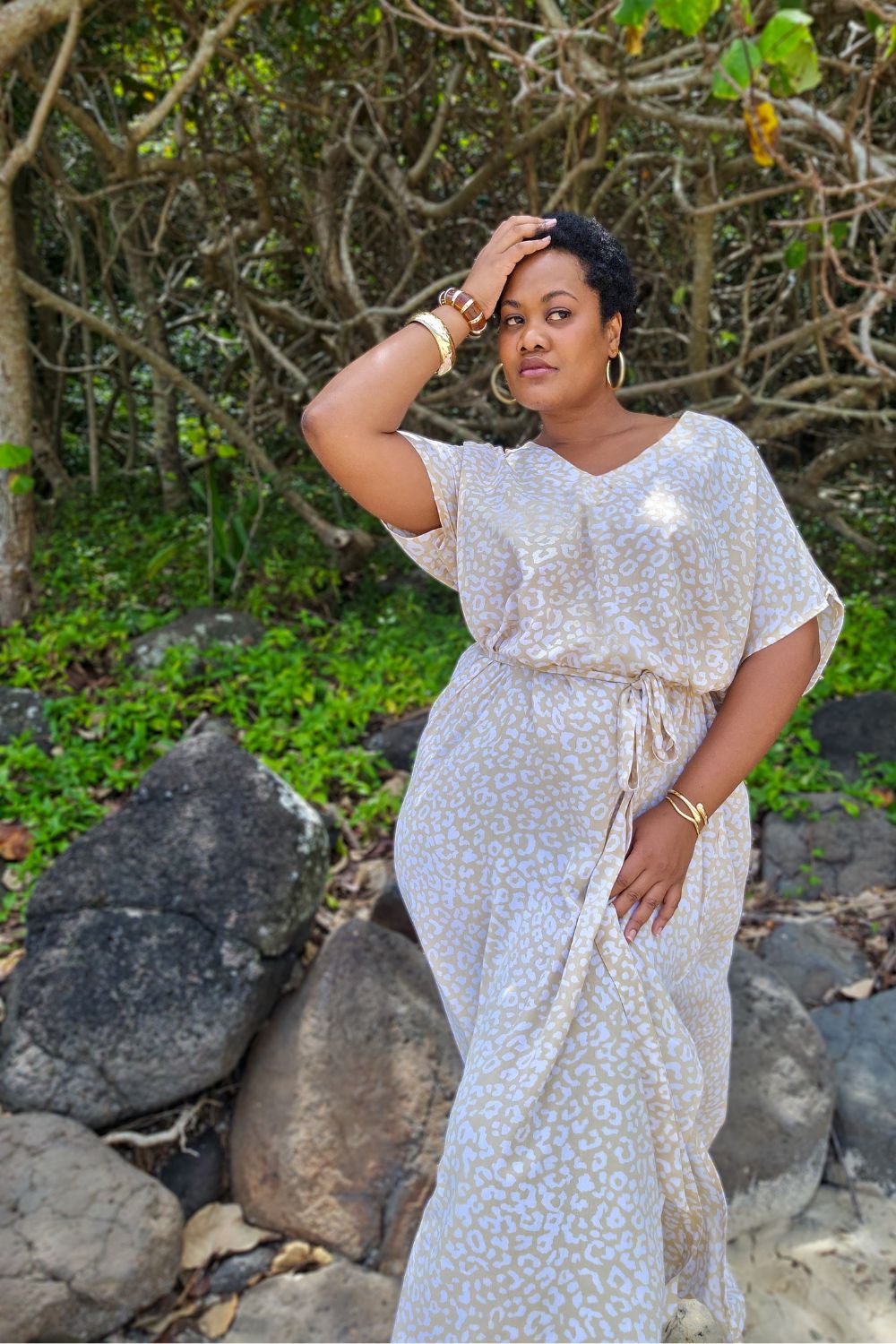 Lady in a white and beige leopard print long summer dress standing among rocks and greenery at the Sunshine Coast