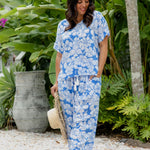 Woman in a blue floral outfit set of relaxed fit pants and summer top standing in a resort garden setting