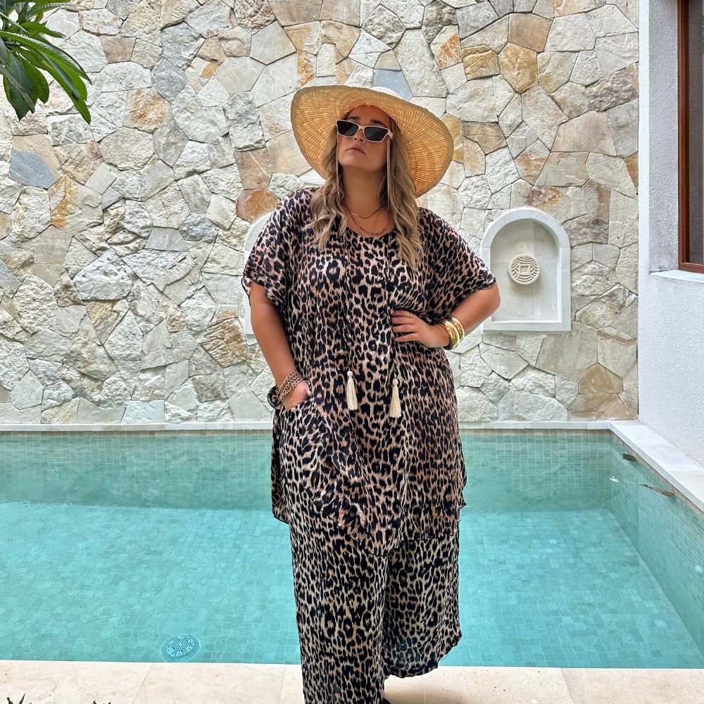 Plus size woman wearing short kaftan dress and wide leg pants in matching leopard in poolside courtyard of Bali villa