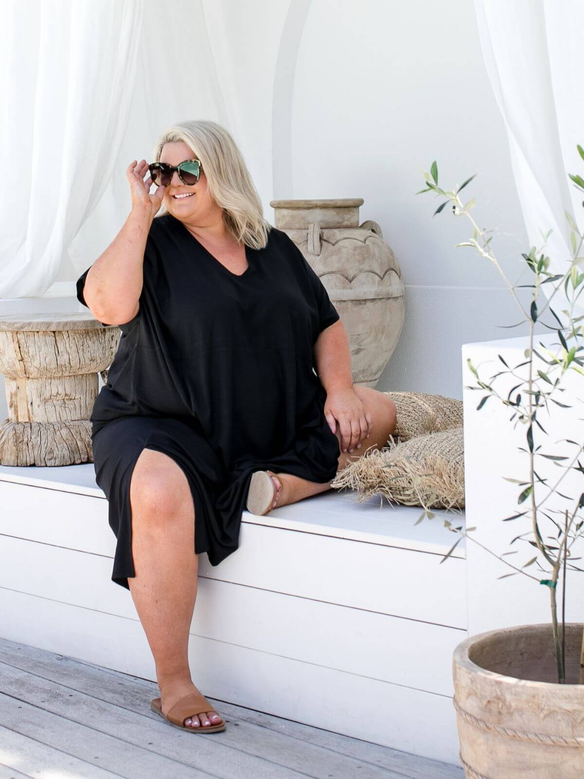 Plus size model wearing black A-line maxi resort dress seated on outdoor deck