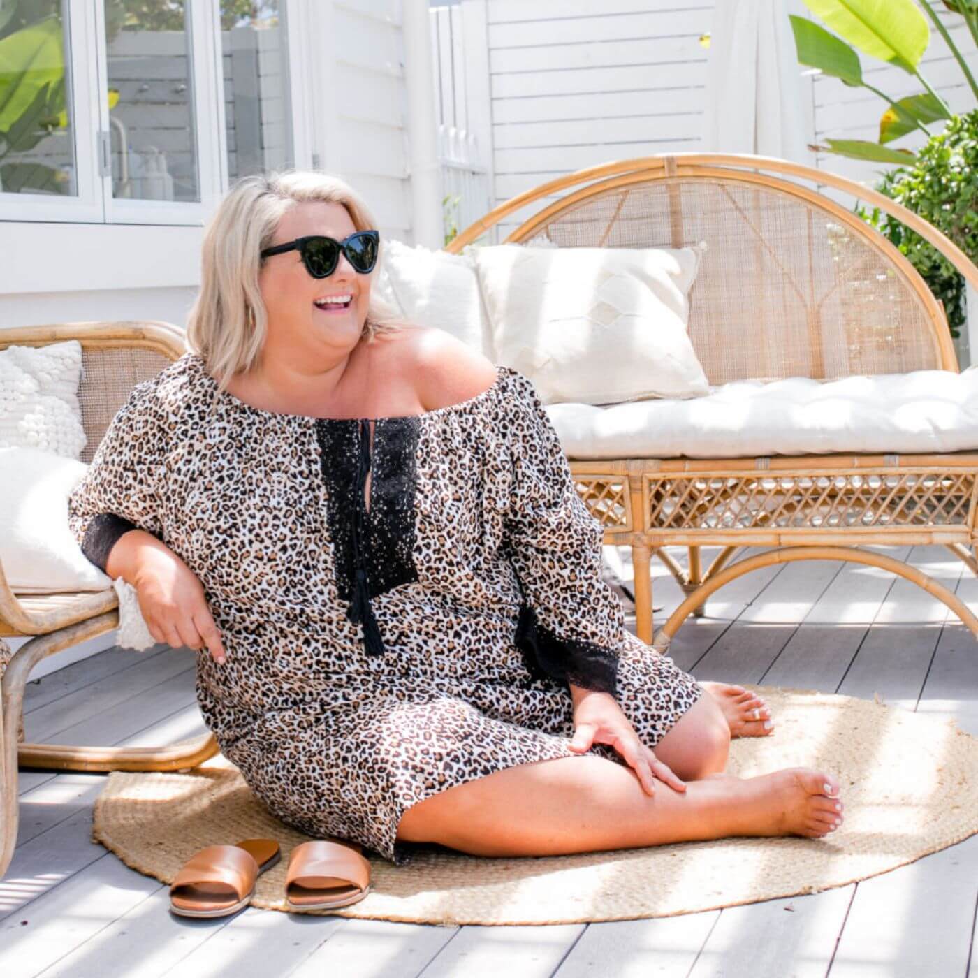 Plus size model wearing a leopard print short kaftan dress sitting on an outdoor balcony with bamboo day beds