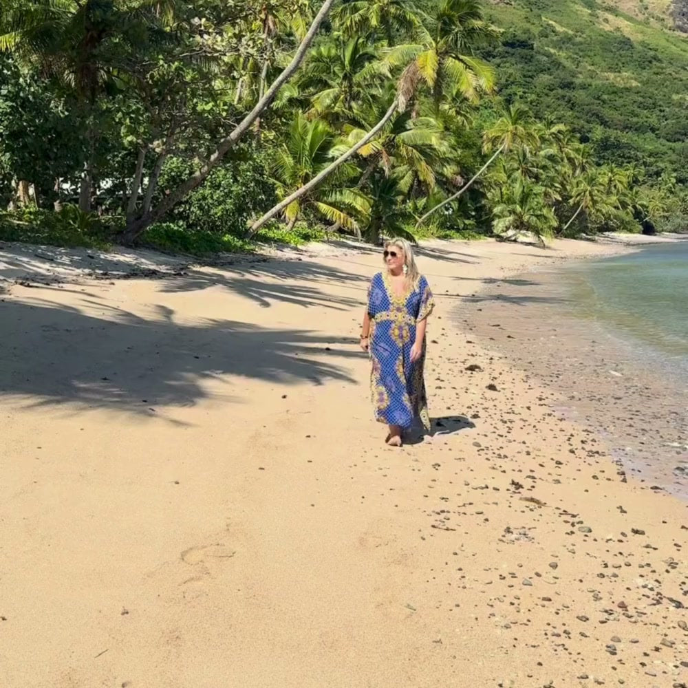 Mature woman walking along a beach in Fiji wearing a blue long kaftan dress.