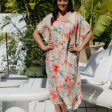 Mature model wearing size small Springtime Kaftan with bold floral print and orange wedges, standing on tropical deck – summer chic resort outfit