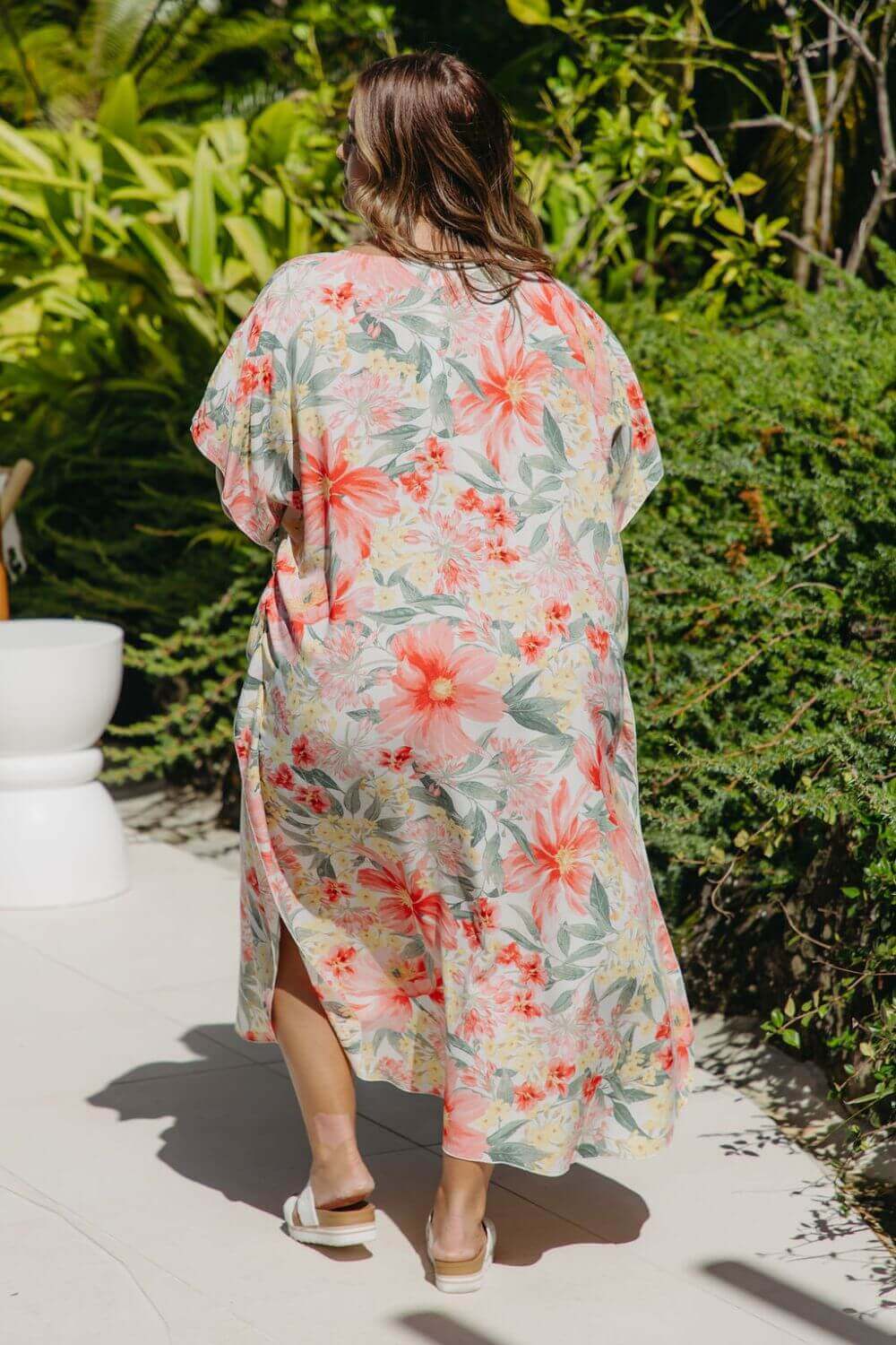 Back view of plus-size model walking poolside in bold floral Springtime Kaftan – white maxi dress with kimono sleeves and side slits