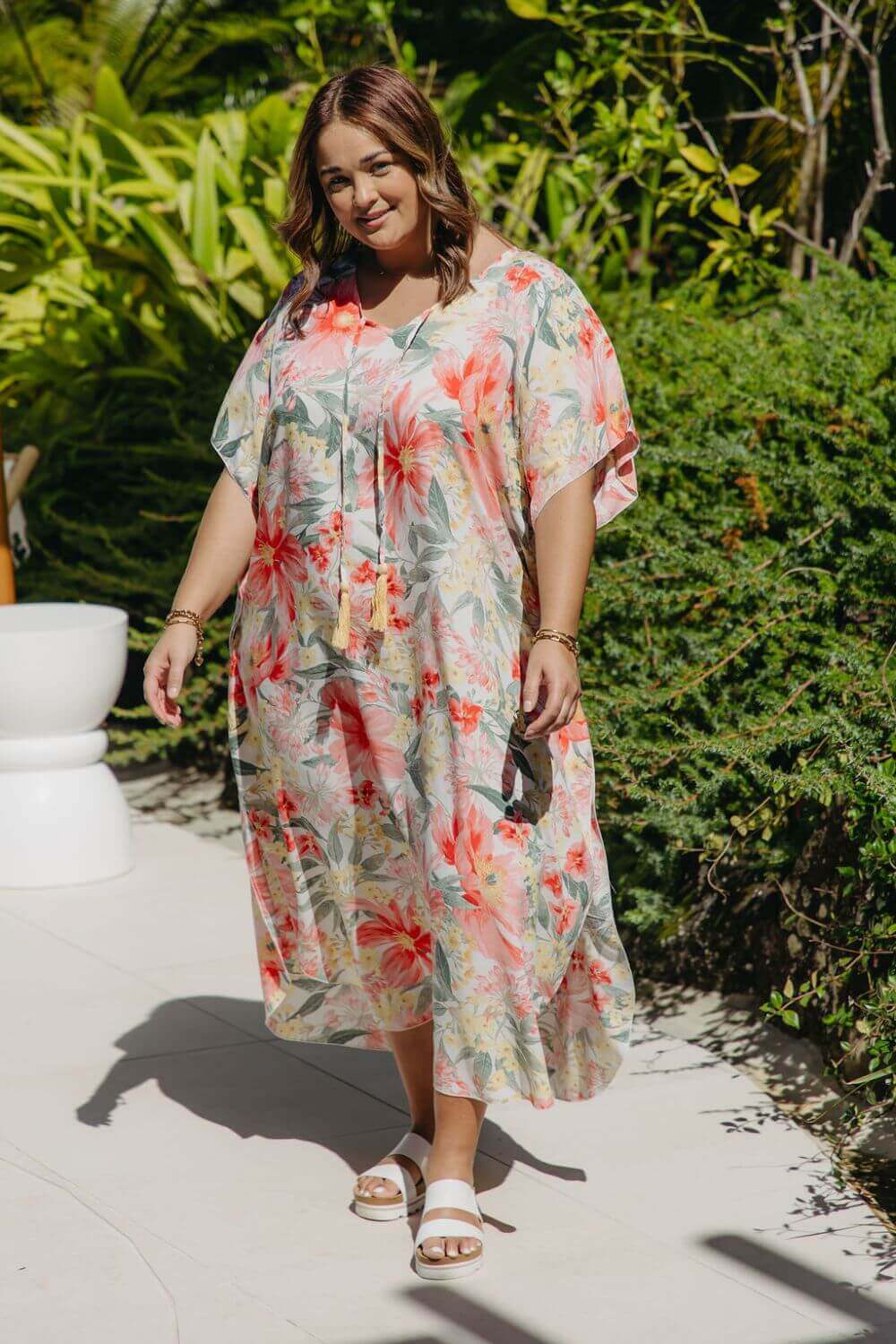 Plus-size model walking poolside in white Springtime Kaftan with bold pink and crimson floral print – breezy summer resort style