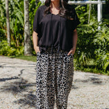A woman wearing a black kaftan top and relaxed fit leopard-print pants in outdoors tropical greenery setting
