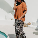 Woman wearing a rust-colored top and leopard print pants by a pool.