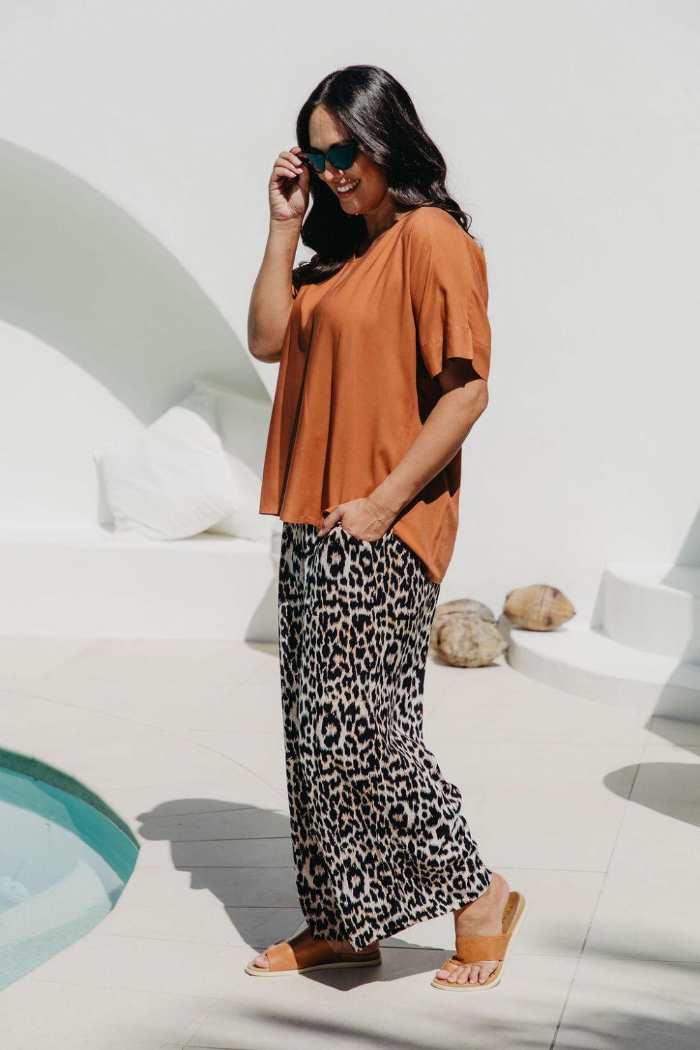 Woman wearing a rust-colored top and leopard print pants by a pool.