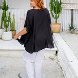 Back view of a woman wearing a black kaftan top walking away, showing length and drape on a size S/M model