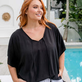 Close-up of a black kaftan top on a size S/M model, styled with a front tuck into white palazzo pants