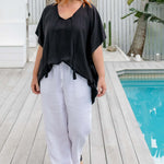 Woman walking poolside wearing a black kaftan top styled with a centre front tuck on a size S/M model