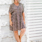 Woman wearing a leopard print dress standing against a white wooden wall.