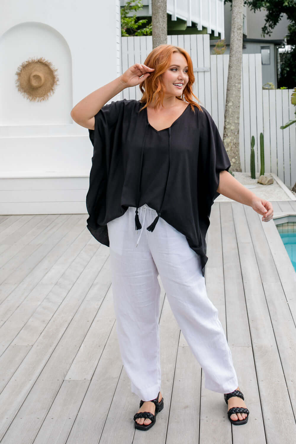 full length view of a woman wearing a black kaftan top half tucked on a pool deck, size S/M model